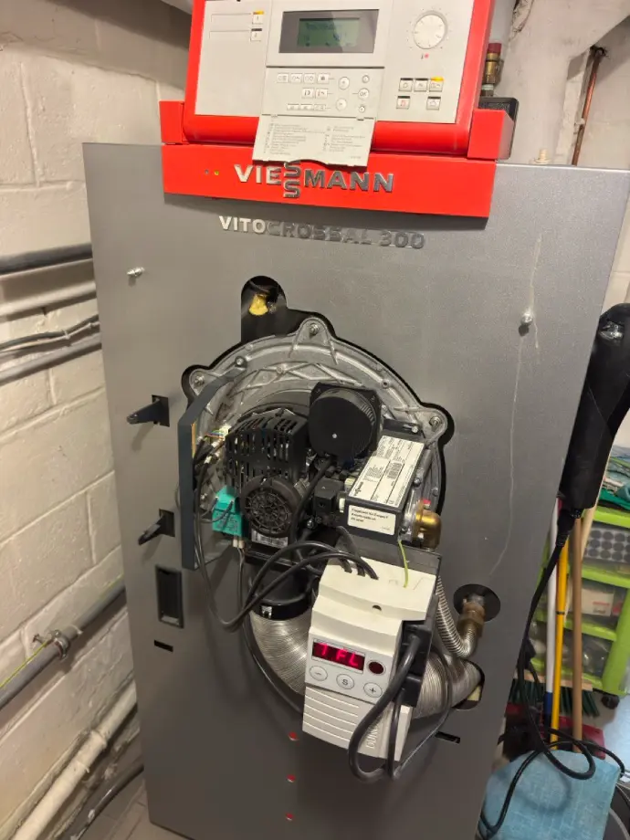 Photo d’une chaudière ouverte avec le brûleur en cours d’entretien. On y voit clairement les composants internes, notamment le brûleur, les conduites et les éléments de sécurité. L’image illustre une opération de maintenance professionnelle, mettant en avant la propreté et la sécurité de l’appareil. Idéal pour un site spécialisé dans le chauffage, l’entretien des chaudières et la maintenance énergétique.